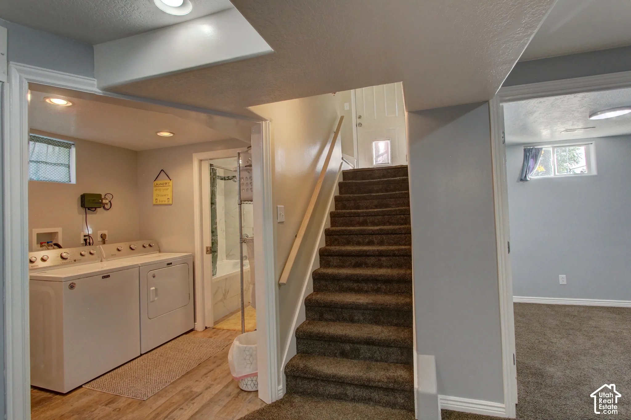 Laundry area featuring wood-finish flooring, recessed lighting, and carpeted staircase with a built-in handrail