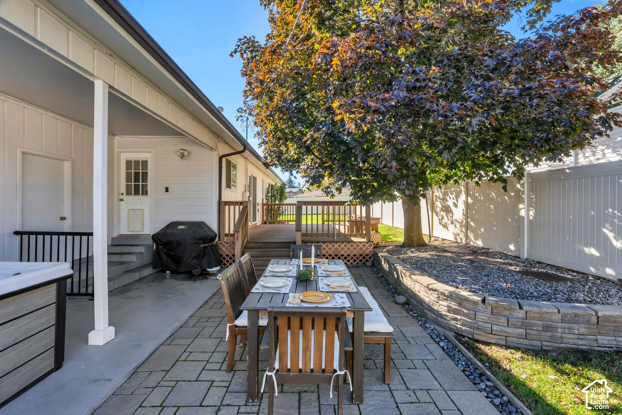 Covered patio with concrete flooring, tiered wooden deck, stone-block retaining wall, and full-height vinyl privacy fencing