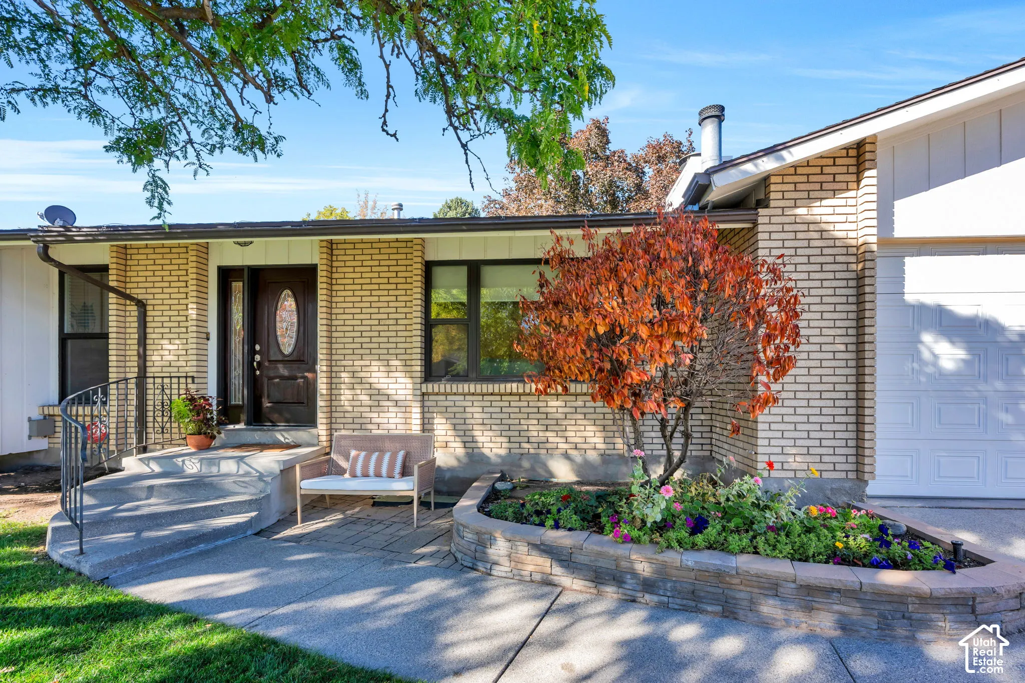 Single-story brick exterior featuring a concrete entry path, decorative wrought iron handrail, stone-block planter, and a multi-paneled front door with an oval glass inset