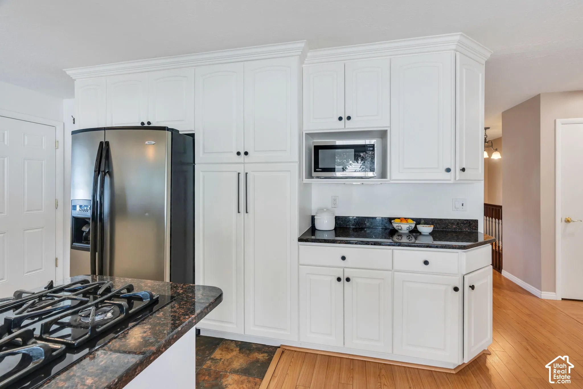 Kitchen featuring white shaker-style cabinetry, dark stone countertops, stainless steel refrigerator, built-in microwave, and wood-finish flooring