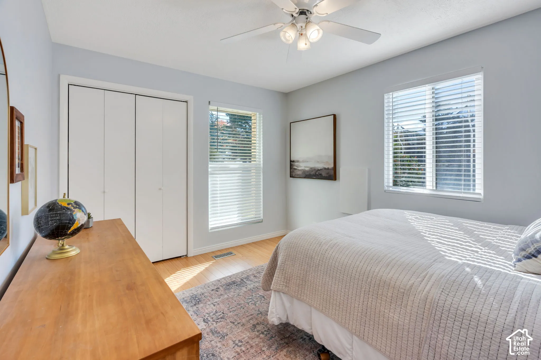 Room featuring wood-finish flooring, dual windows with horizontal blinds, bi-fold closet doors, and a ceiling fan with integrated lighting