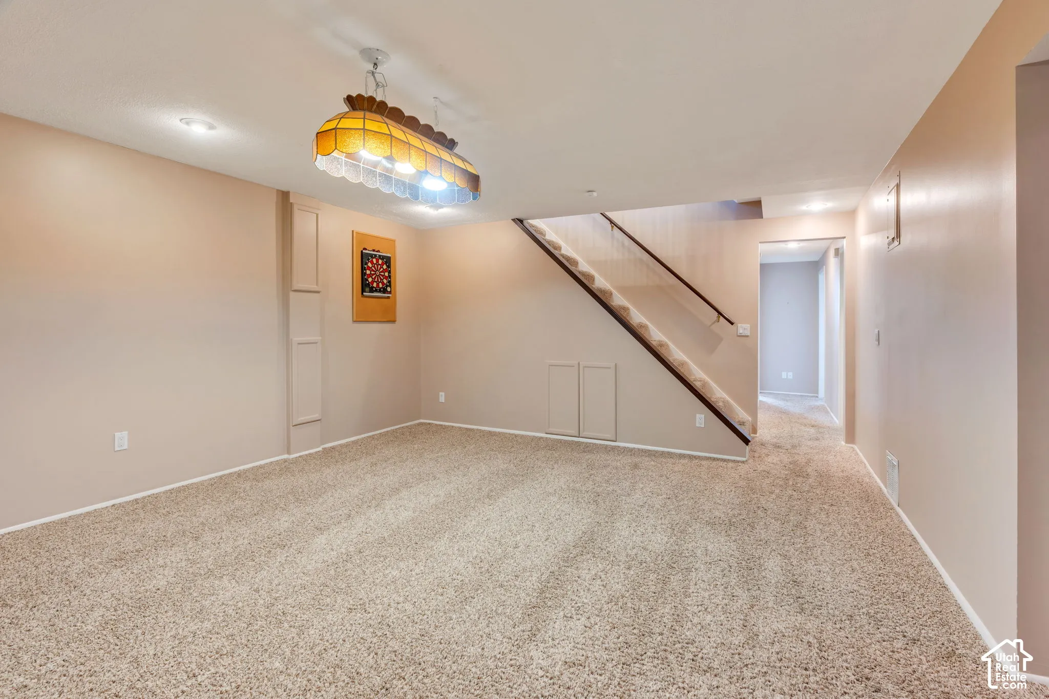 Neutral wall palette with carpeted flooring, staircase featuring a wooden handrail, and decorative multi-light pendant fixture