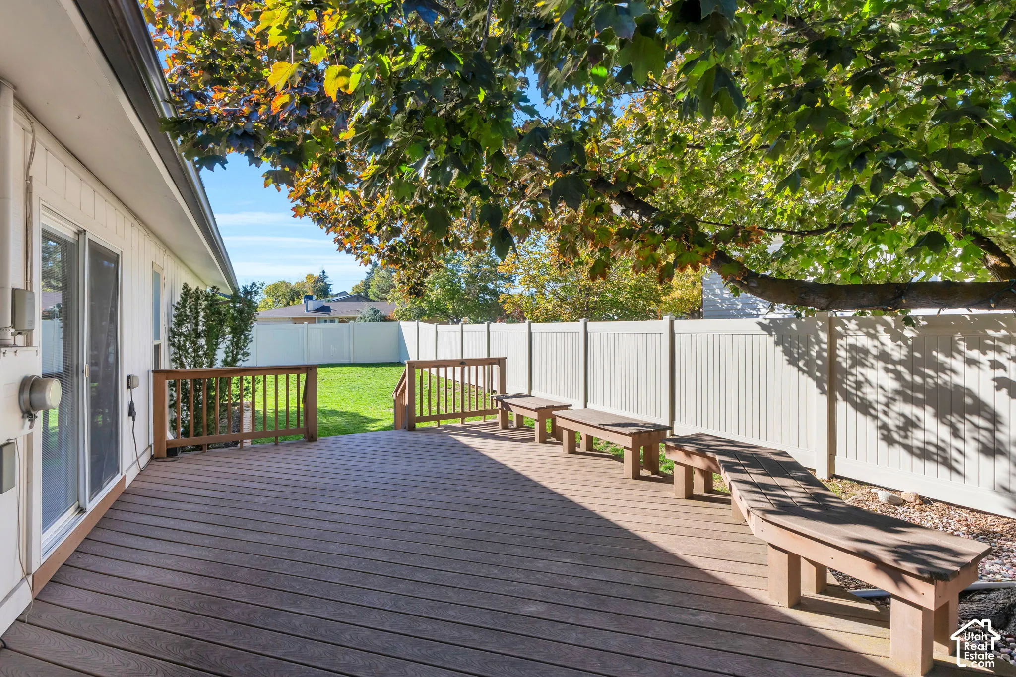 Backyard deck featuring composite wood-finish decking, integrated built-in benches, perimeter vinyl fencing, and a mature tree canopy