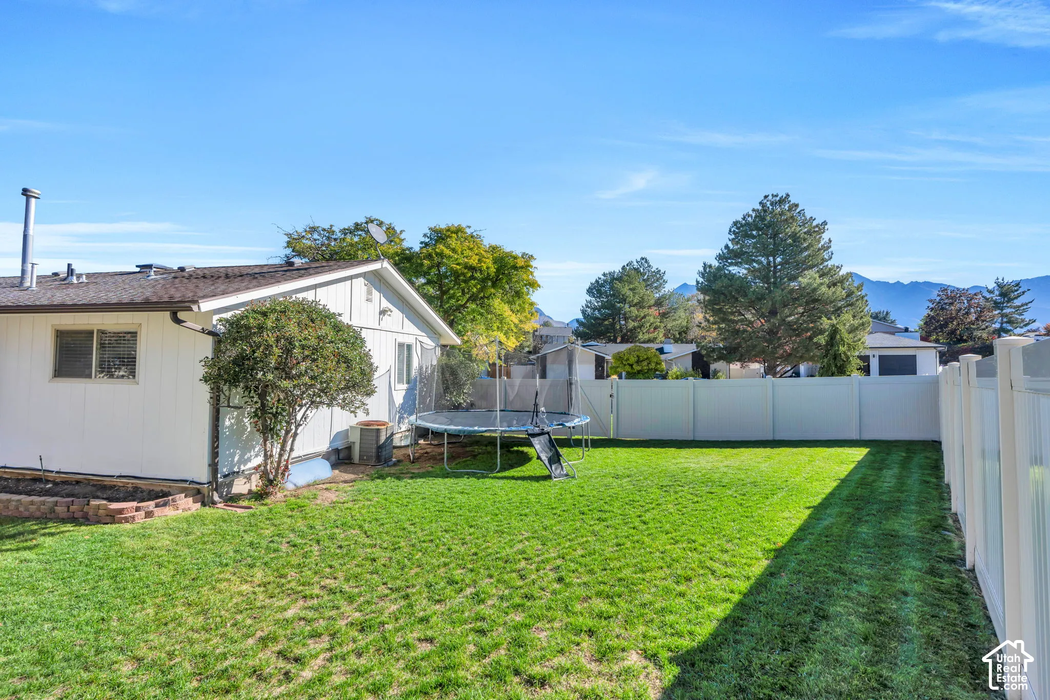 Backyard featuring a manicured lawn, white vinyl fencing, raised landscape border, and mountain backdrop