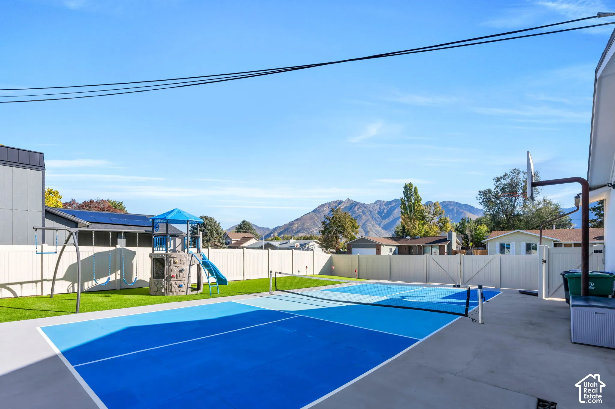 Private backyard featuring a hard-surfaced pickleball court, synthetic turf lawn, perimeter vinyl fencing, and mountain scenery