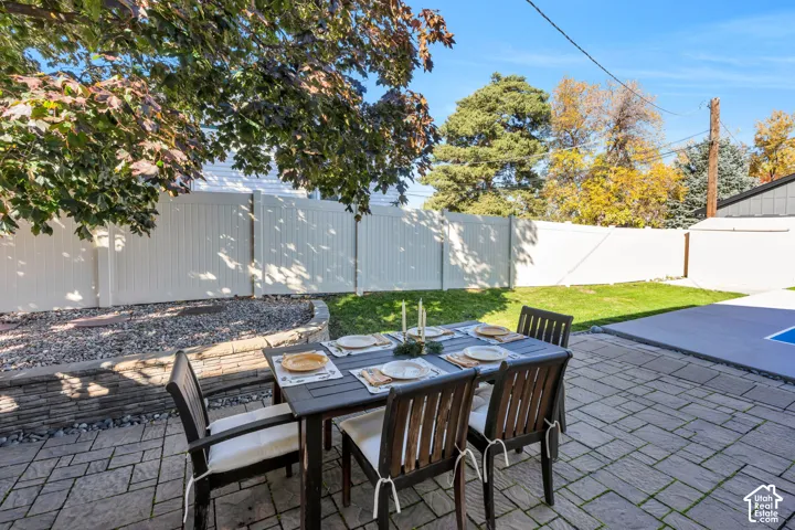 Backyard featuring a paved stone patio, retaining wall with gravel landscaping, privacy fencing, and mature trees