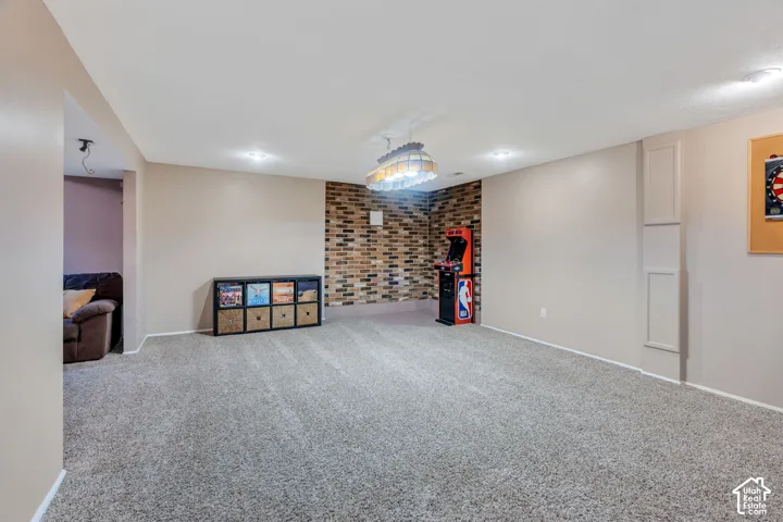 Interior room featuring a textured brick accent wall, neutral carpeting, recessed ceiling lighting, and a multi-light decorative pendant fixture