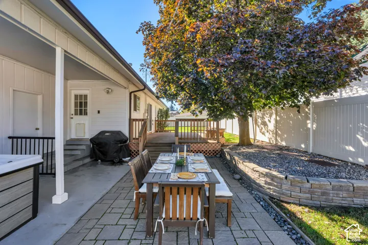 Covered patio with concrete flooring, tiered wooden deck, stone-block retaining wall, and full-height vinyl privacy fencing