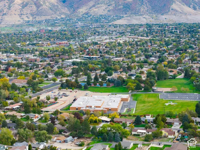Aerial perspective highlighting a sprawling residential community set against a prominent mountain backdrop, featuring expansive green spaces, established tree canopy, and proximity to paved recreation facilities