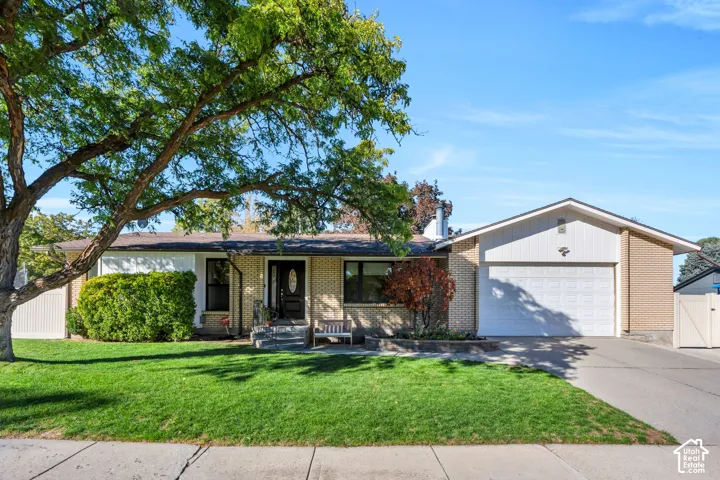 Single-level brick exterior featuring a multi-paneled garage door, front entryway with a decorative glass-insert door, concrete driveway, and mature landscaping
