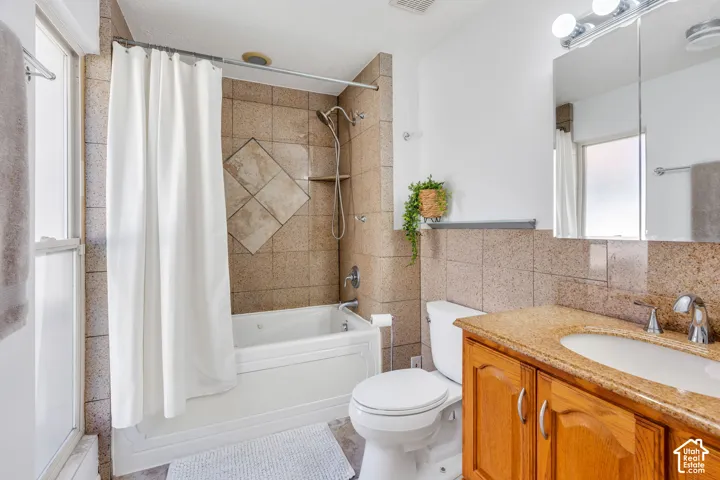 Bathroom featuring a jetted soaking tub with a shower-head assembly, tile surround, vanity with a stone-finish countertop and integrated sink, and a mirrored medicine cabinet
