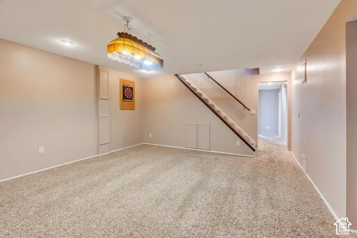 Neutral wall palette with carpeted flooring, staircase featuring a wooden handrail, and decorative multi-light pendant fixture