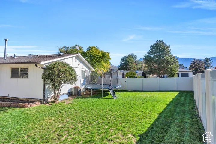 Backyard featuring a manicured lawn, white vinyl fencing, raised landscape border, and mountain backdrop