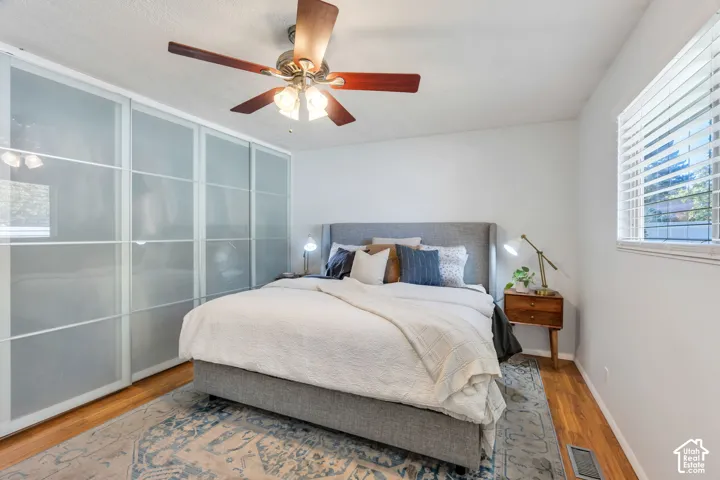 Frosted glass sliding wardrobe doors, wood-finish flooring, ceiling fan with integrated light fixture, and horizontal window blinds