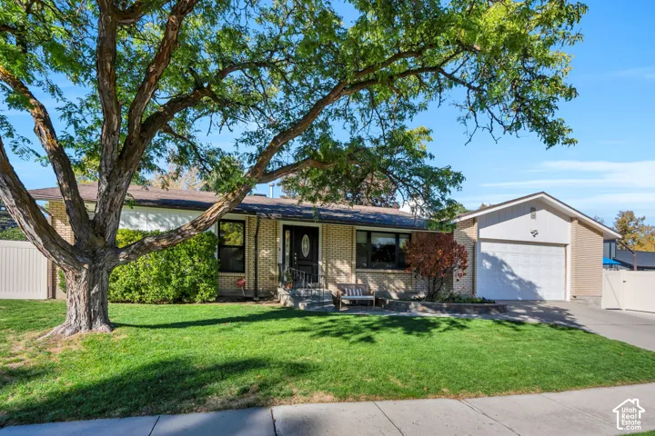Single-story brick exterior featuring a low-pitch roofline, attached two-car garage, mature landscaping, and white privacy fencing