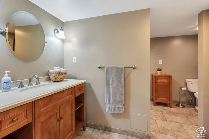 Bathroom featuring a wood vanity with integrated shelving, a solid-surface countertop, an oval wall-mounted mirror, brushed nickel-finish faucet, and tiled flooring