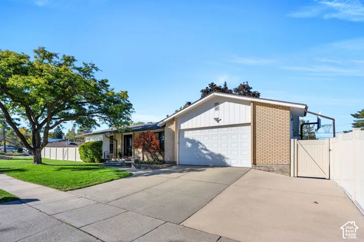 Single-level residence featuring a brick and vertical siding exterior, attached two-car garage, concrete driveway, and white vinyl privacy fencing