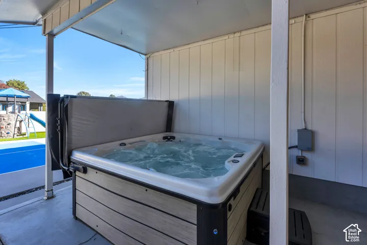 Covered outdoor patio area featuring a built-in hot tub with wood-finish siding, white vertical panel siding, and concrete flooring