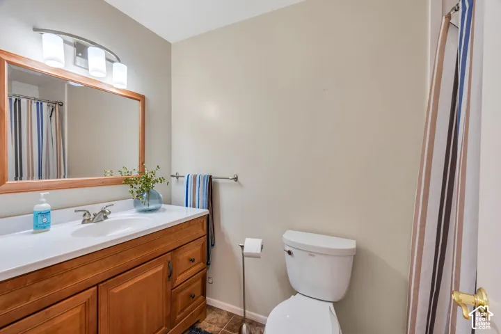 Bathroom featuring a wood-finish vanity with an integrated countertop, oval basin, three-light curved fixture, framed mirror, and tile flooring