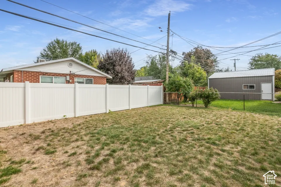 Rear yard featuring a white vinyl privacy fence, detached metal-sided storage structure, and brick exterior finish