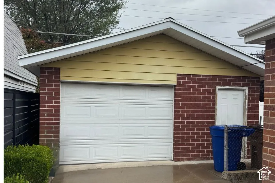 Detached garage featuring red brick masonry, horizontal siding, a gabled roofline, and a panel-style overhead door with a separate service entry