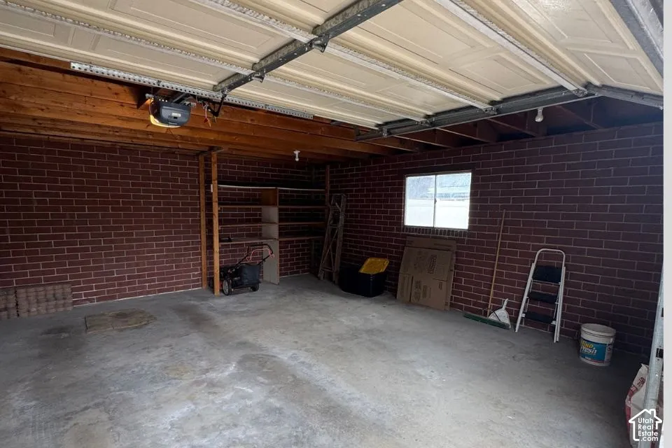 Attached garage featuring exposed brick walls, a concrete floor, an overhead sectional door, and built-in timber shelving