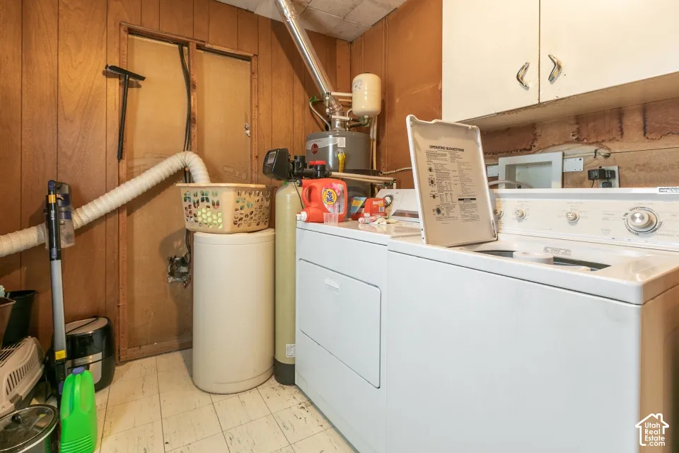 Utility area featuring wood-panel wall finish, white upper cabinetry, a water softening system, and a tank-style water heater