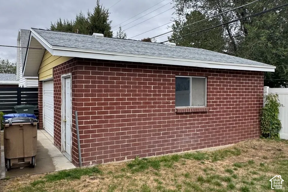 Detached garage featuring red brick masonry, a gable roof with asphalt shingles, a white metal pedestrian door, and a sliding window