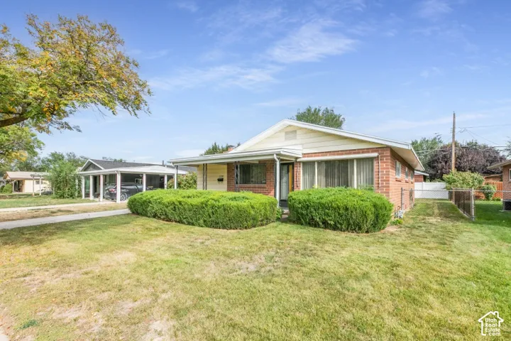 Rambler-style exterior featuring a brick and siding facade, covered front porch, and expansive front lawn with mature landscaping