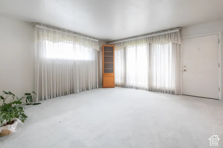 Neutral interior space featuring expansive windows, neutral wall-to-wall carpeting, and a built-in corner cabinet