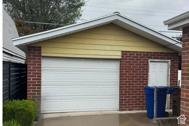 Detached garage featuring red brick masonry, horizontal siding, a gabled roofline, and a panel-style overhead door with a separate service entry