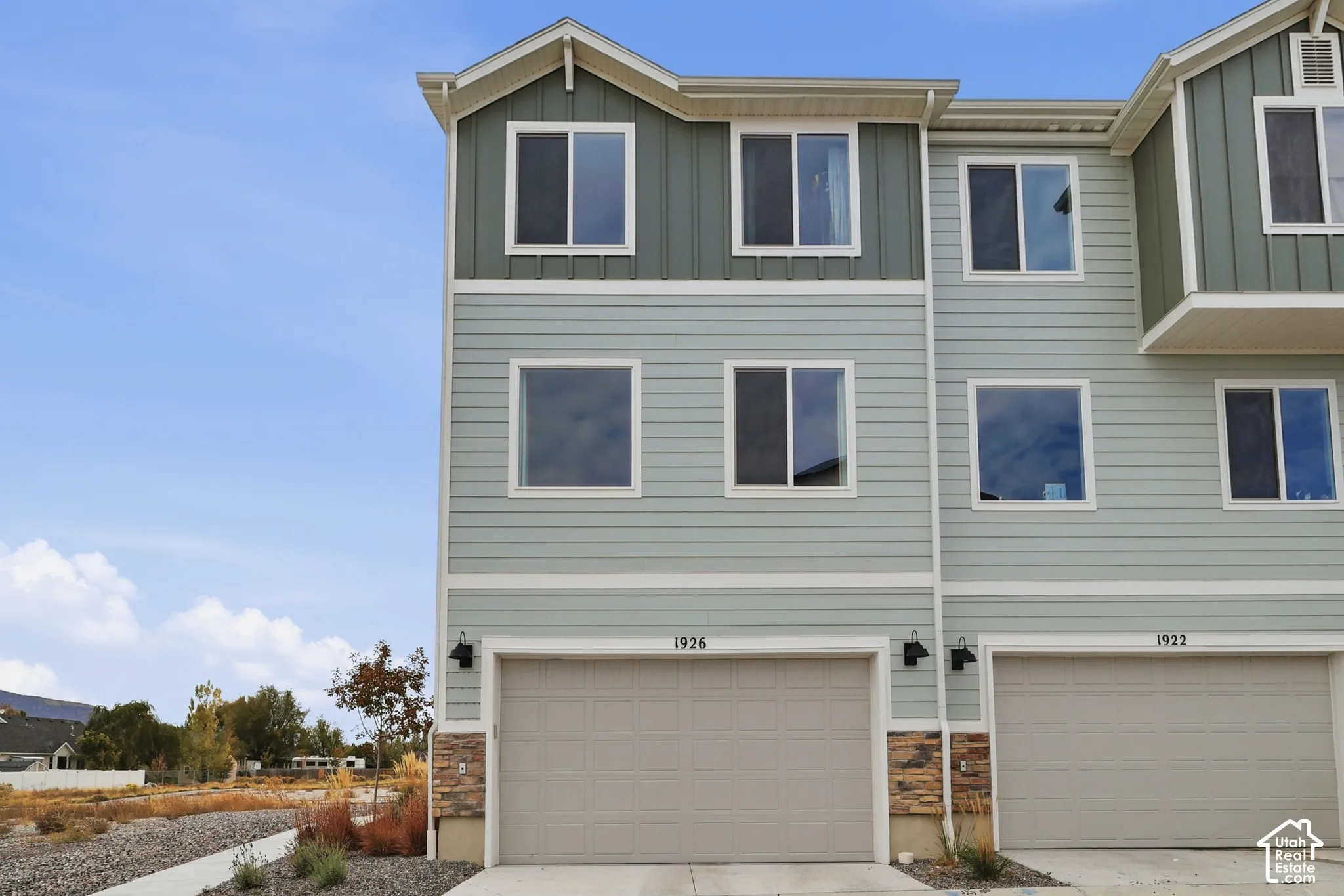 Three-story townhome exterior featuring horizontal lap siding, vertical board-and-batten gable accents, stone veneer foundation detailing, and an attached multi-car garage with overhead doors
