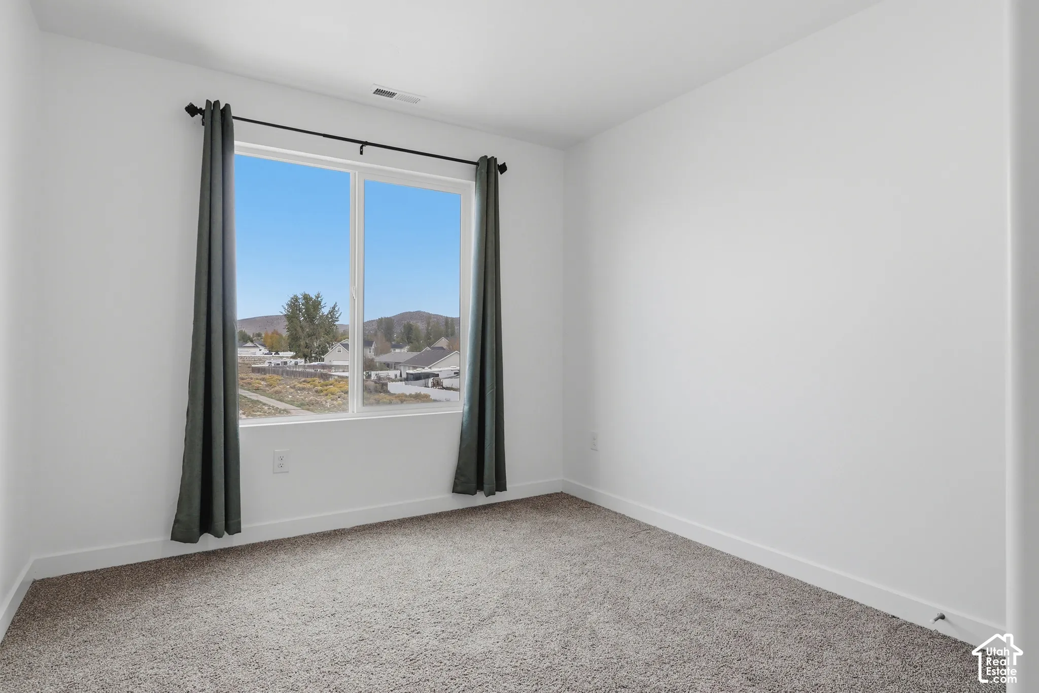 Neutral-toned interior space featuring neutral carpeting, white walls, and a sliding window with mountain scenery