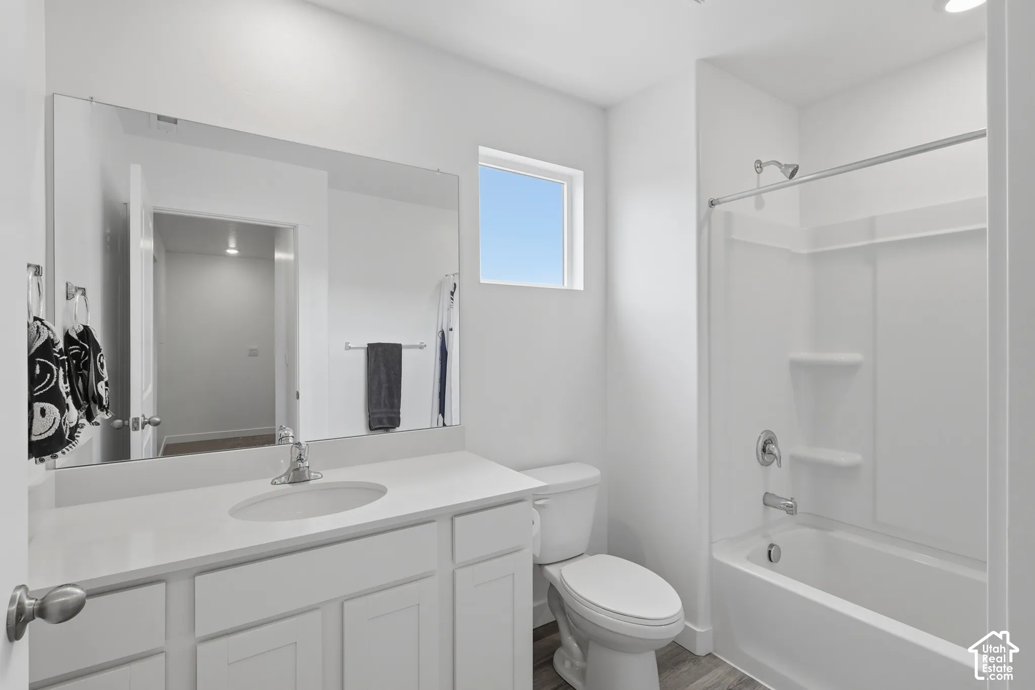 Bathroom featuring a vanity with a white countertop and oval under-mount sink, full-width mirror, white cabinetry, and a tub-shower combination with integrated shelving