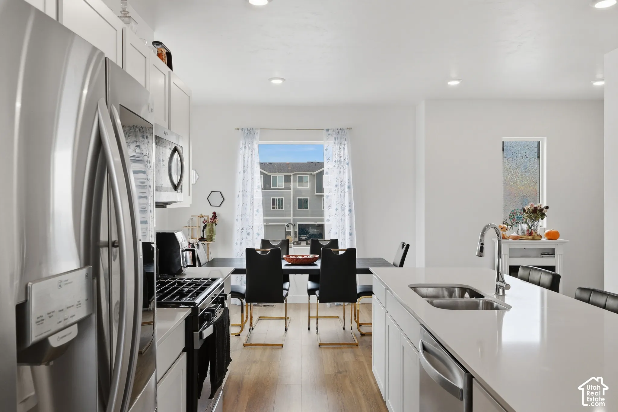 Kitchen featuring white cabinetry, quartz countertops, a dual-basin stainless steel sink with a high-arch faucet, stainless steel appliances, and wood-finish flooring