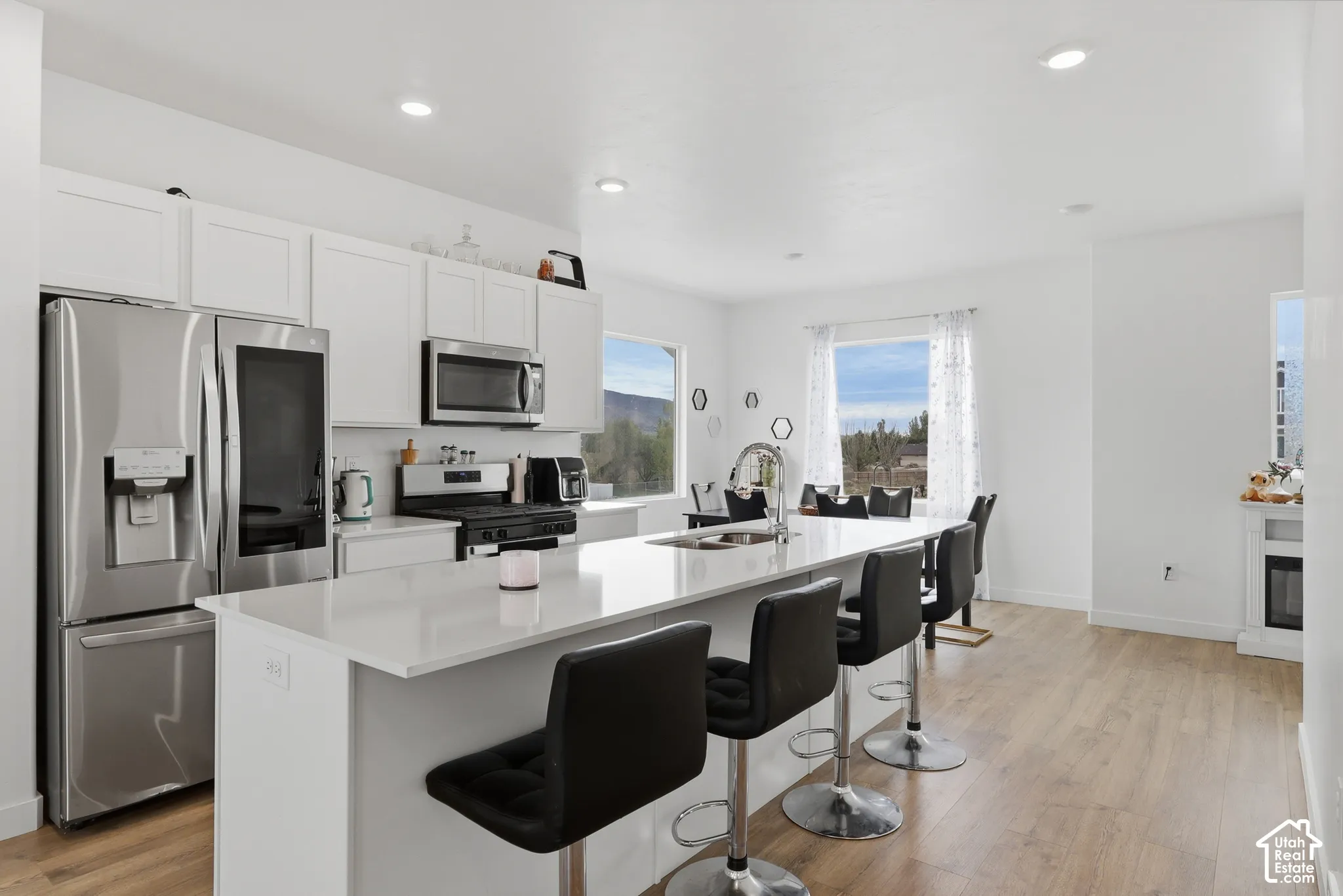 Kitchen featuring white cabinetry, an expansive central island with a solid-surface countertop, stainless steel appliances, recessed lighting, and wood-finish flooring