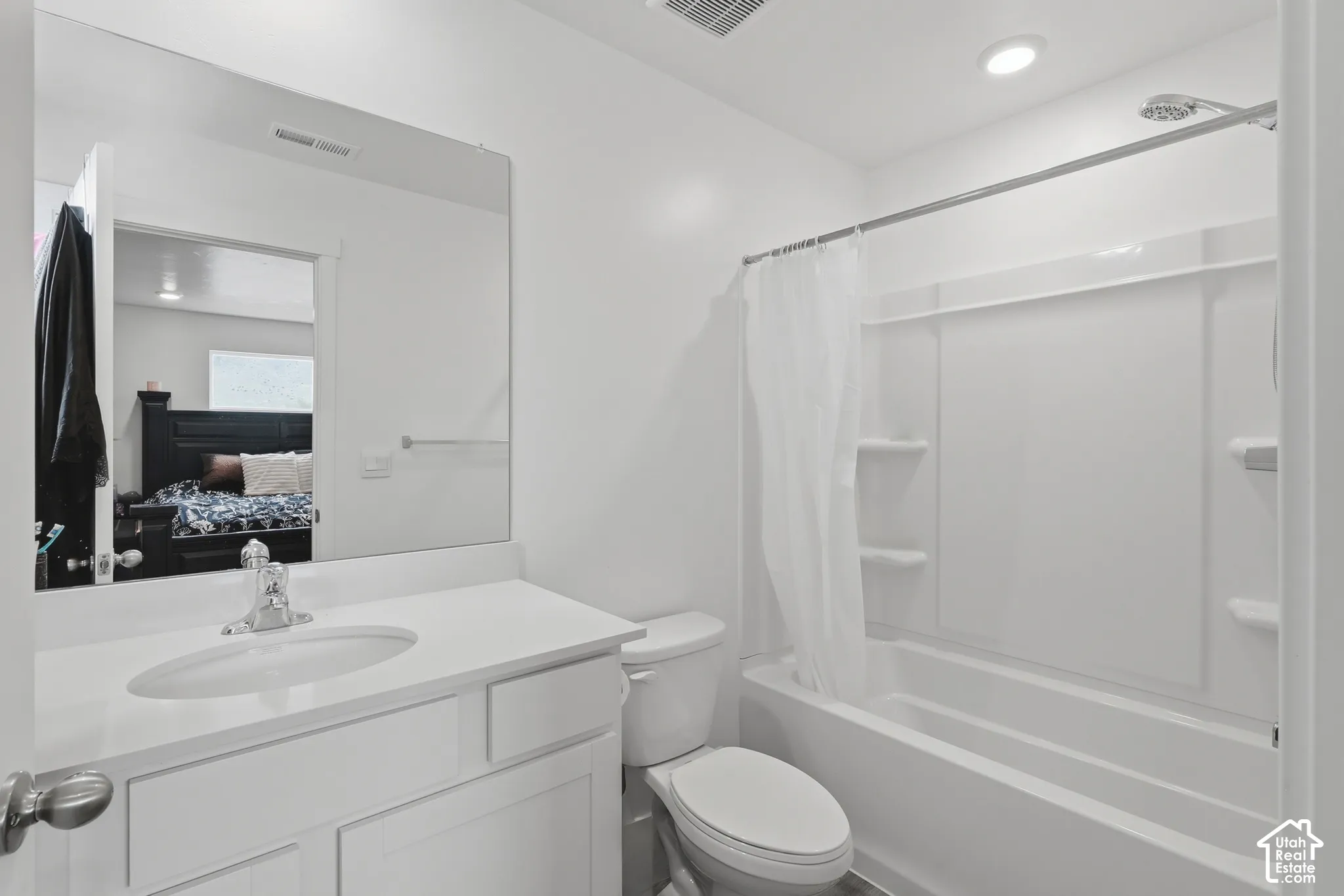 Bathroom featuring a white vanity with an integrated countertop sink, chrome faucet, wall-to-wall mirror, and a shower-tub combination with built-in shelving