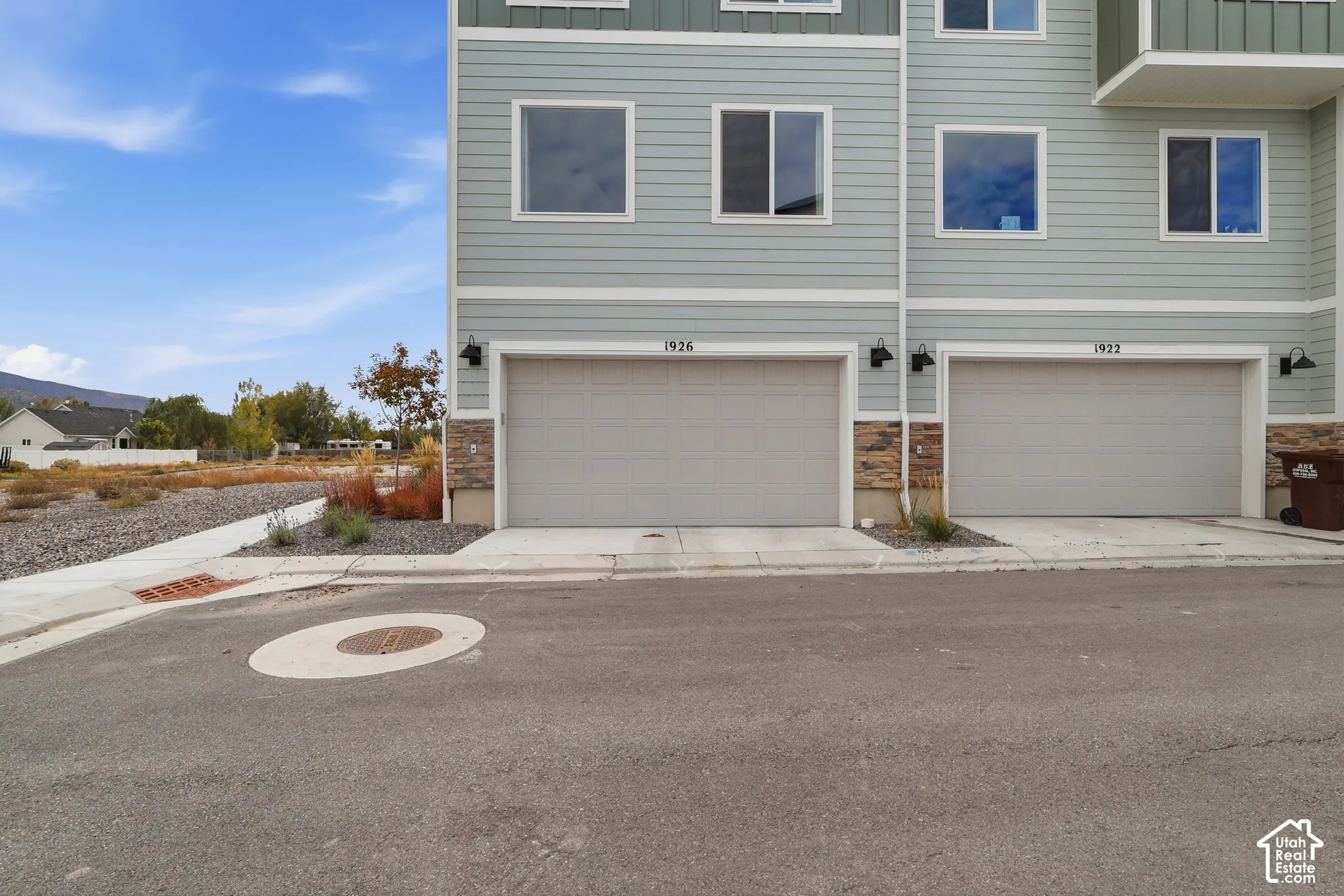 Exterior facade featuring horizontal siding, stone veneer accents, two-car garage doors, and wall-mounted exterior lighting fixtures