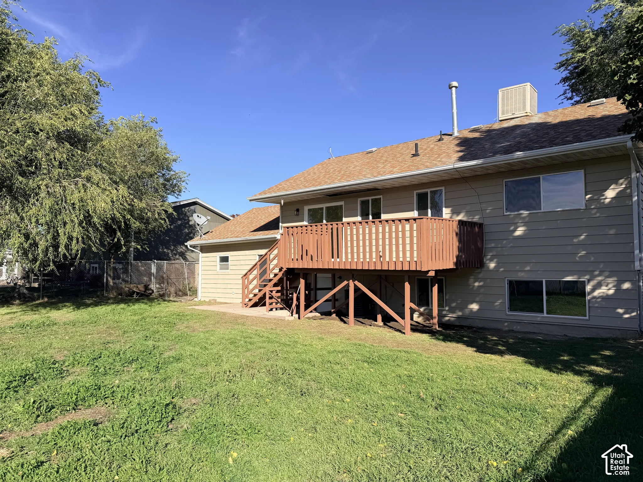 Rear exterior featuring horizontal lap siding, an elevated wood deck with stairs, a concrete patio, and a chain-link fence