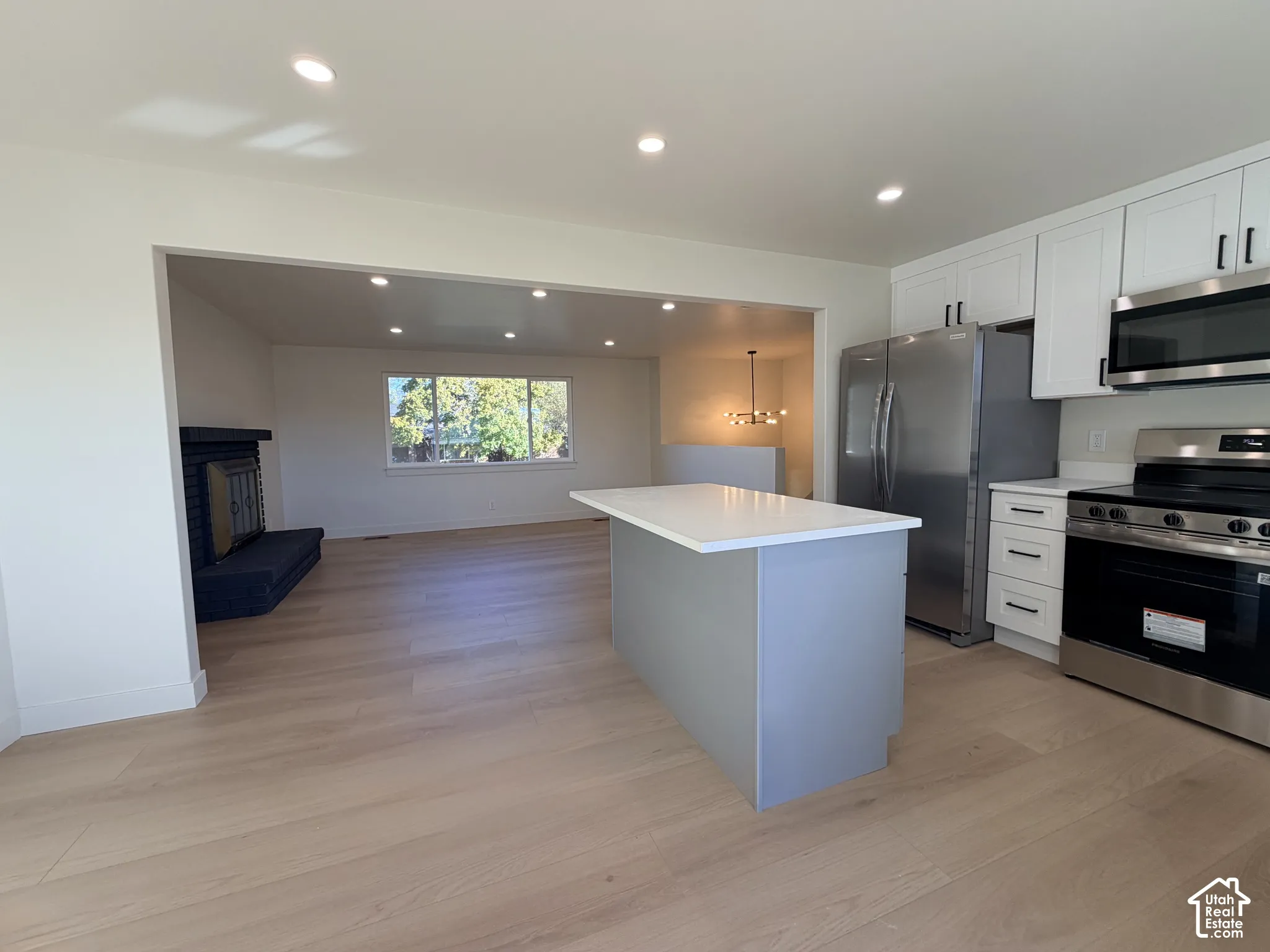Kitchen featuring white Shaker-style cabinetry, a central island with a quartz countertop, stainless steel appliances, recessed lighting, and wood-finish flooring