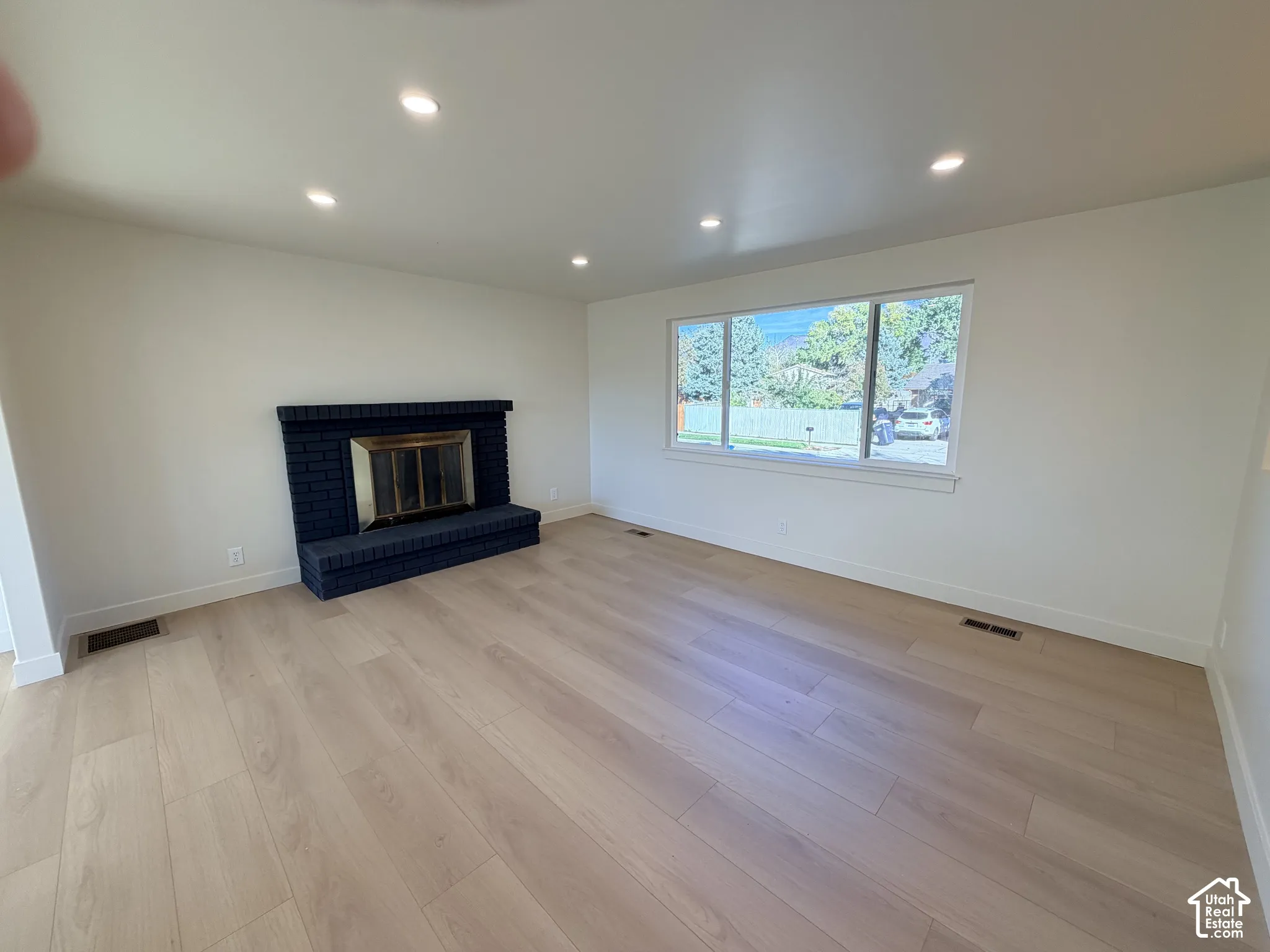 Living area featuring light-toned wood-finish flooring, recessed lighting, and a painted brick fireplace with a metal insert