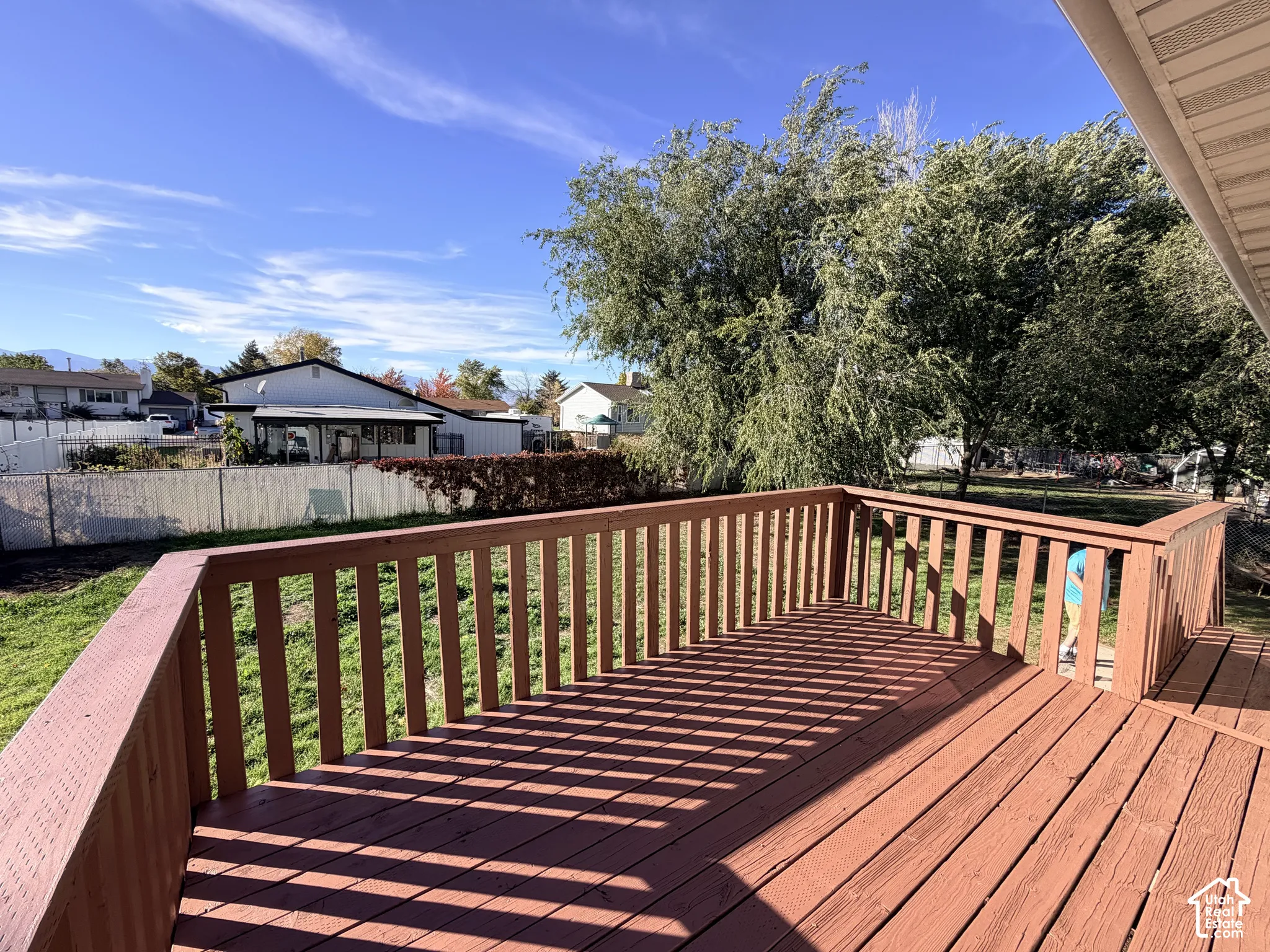 Raised wooden deck featuring vertical balusters, an expansive lawn, and mature trees