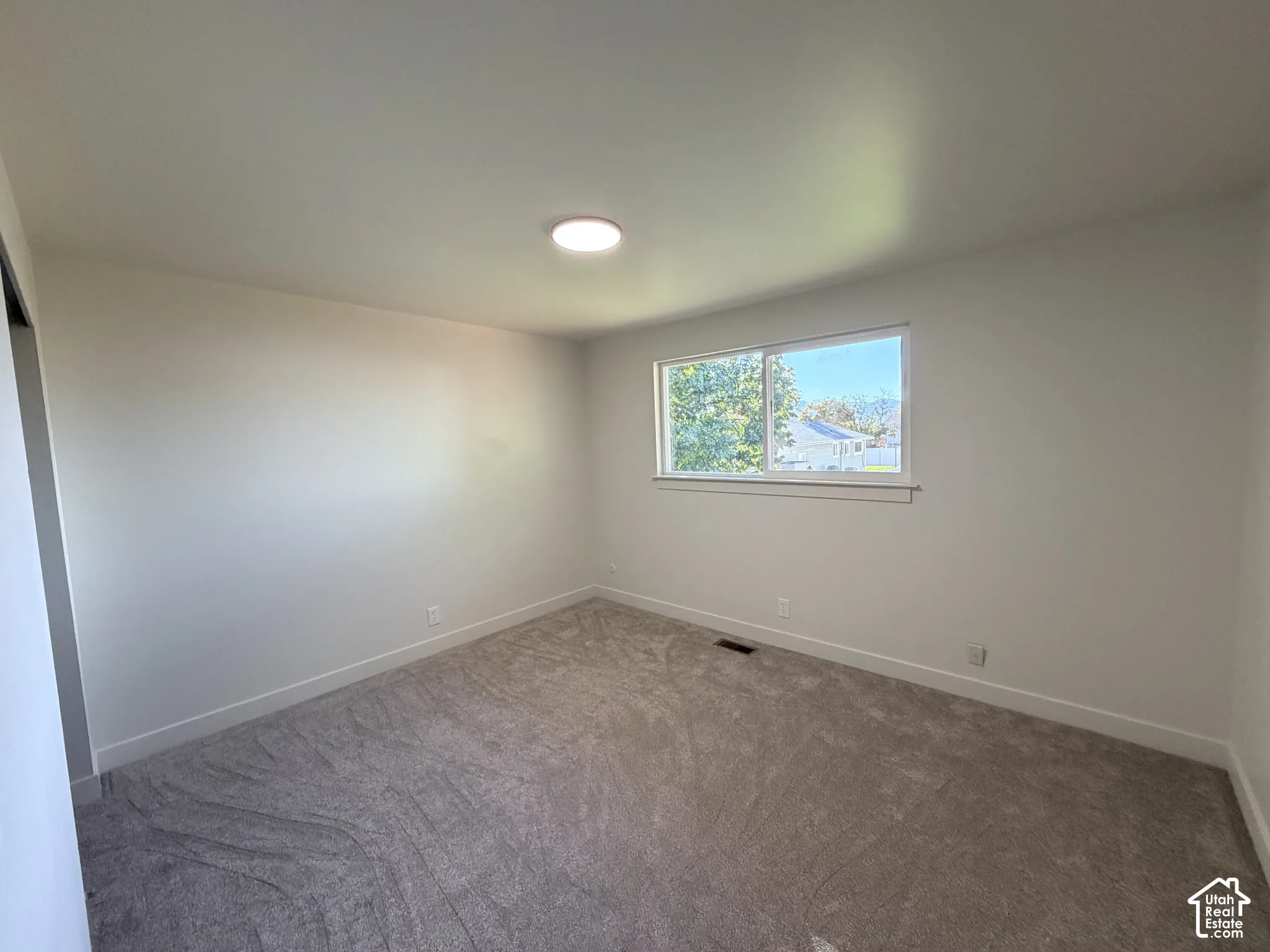 Neutral interior space featuring carpeted flooring, a single-pane horizontal window, and a flush-mount overhead light fixture