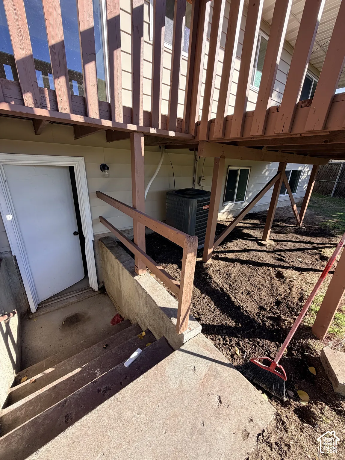 Raised wood deck featuring vertical wood balusters and structural supports, exterior door with concrete staircase, and central air conditioning unit