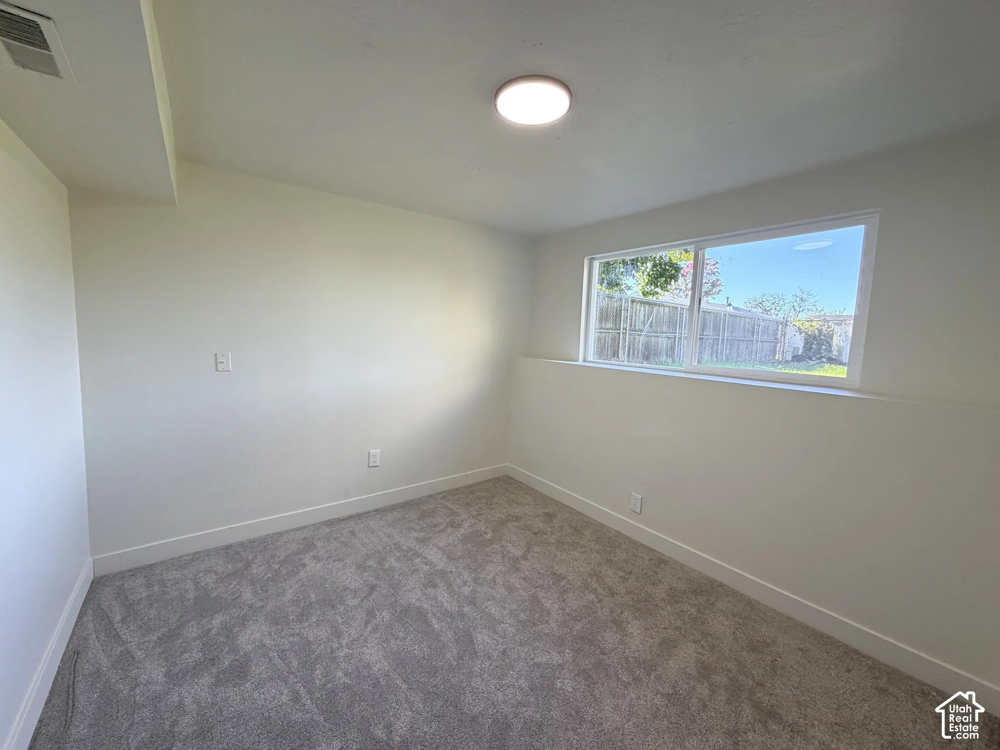 Neutral interior space featuring neutral wall-to-wall carpeting, crisp white wall finishes, a sliding window with exterior sill, and a flush-mount overhead light fixture