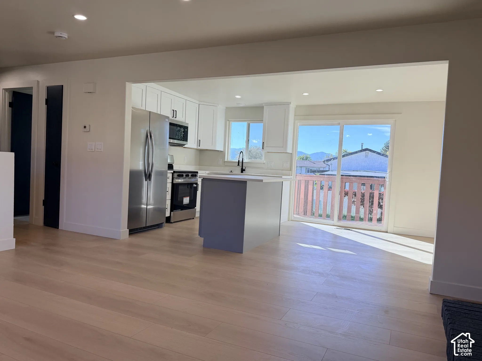 Kitchen featuring white cabinetry, center island, stainless steel appliances, and wood-finish flooring, accompanied by sliding glass doors
