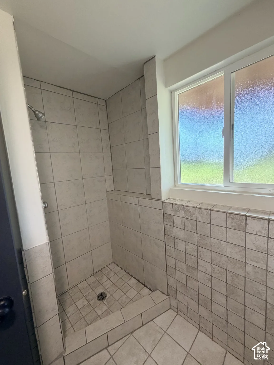 Walk-in shower enclosure featuring floor-to-ceiling neutral ceramic tile, a dedicated shower head, and an operable window with privacy glass