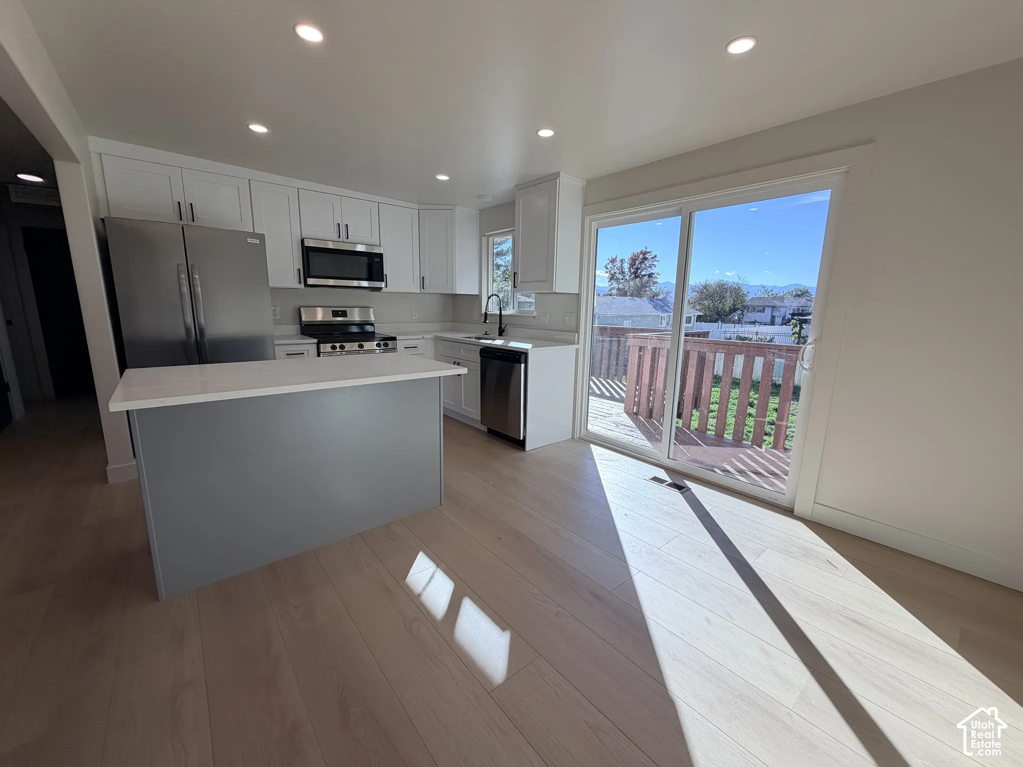 Kitchen featuring white shaker-style cabinetry, quartz countertops, stainless steel appliances, an island with a grey base, and wood-finish flooring