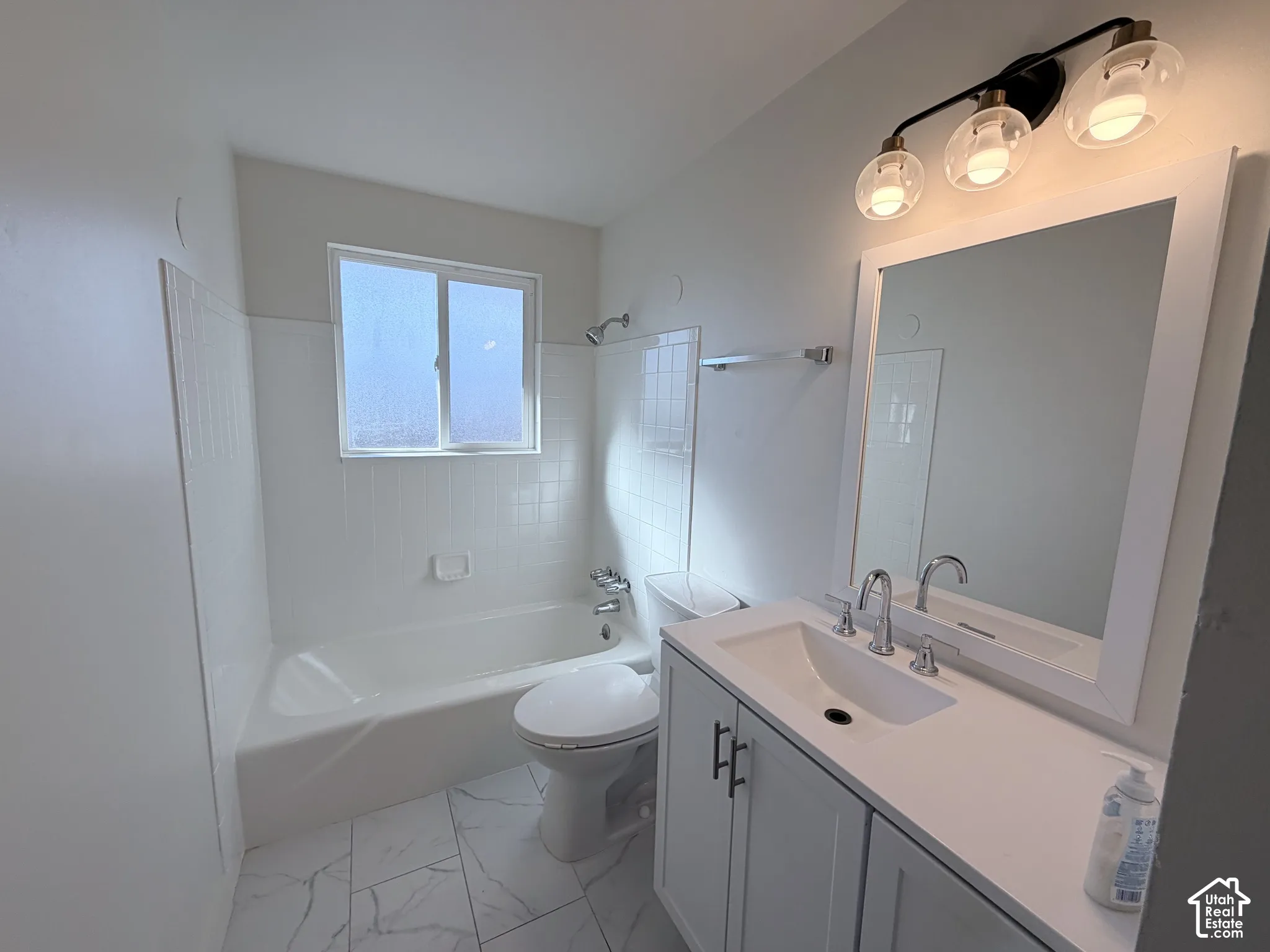 Bathroom featuring a vanity with white cabinetry, a solid-surface countertop with an integrated sink, polished chrome fixtures, white tile tub surround, and marble-finish floor tiling