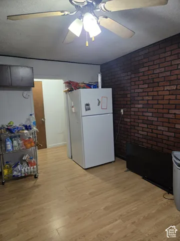 Interior space featuring a dark-toned brick accent wall, wood-finish flooring, and a ceiling-mounted light fixture with a multi-blade fan